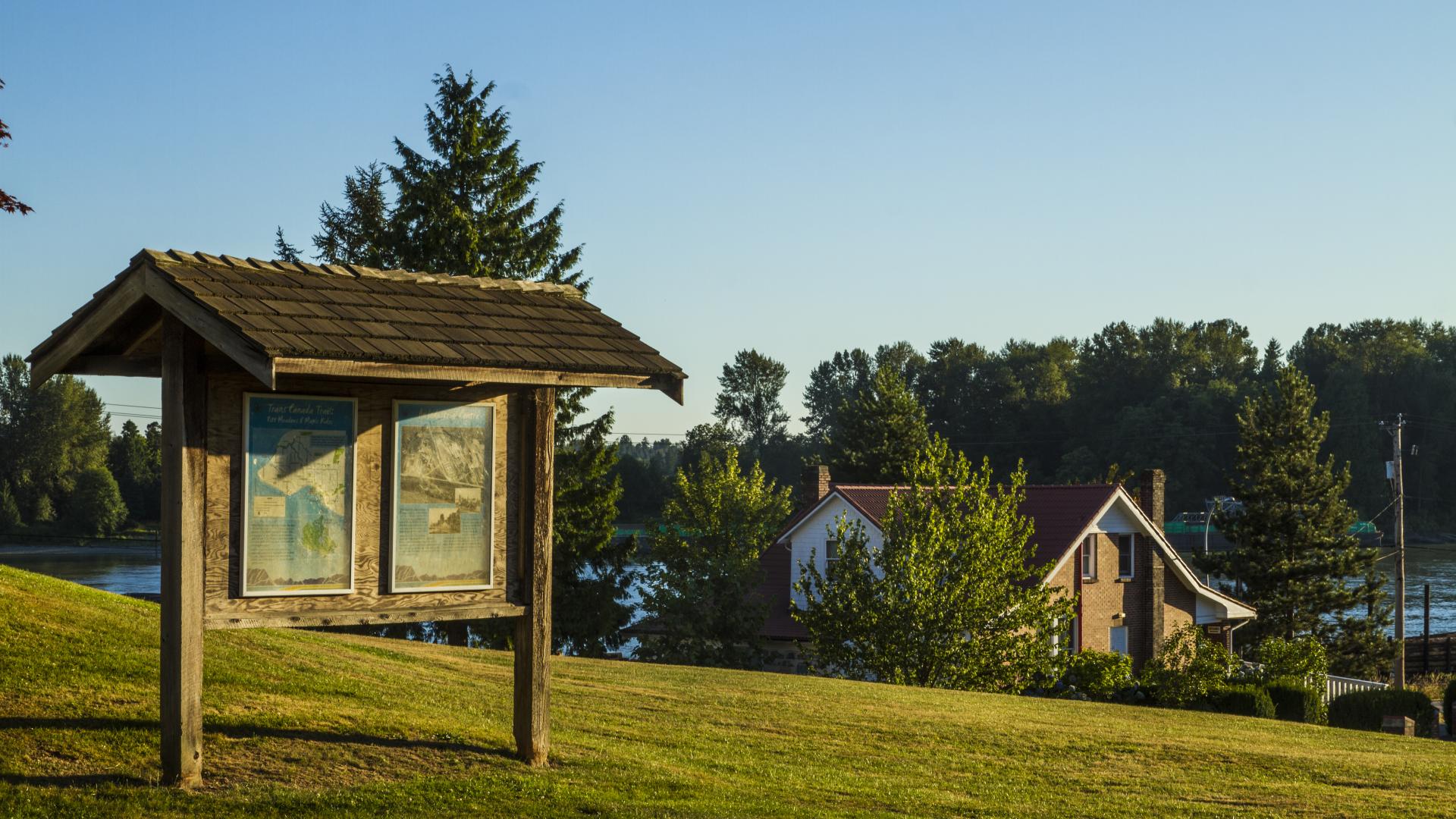 A grassy hill with houses at the bottom. There is a large wood sign with a small roof on the hill.